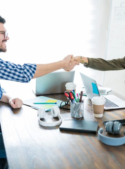 Smiling business partners shaking hands after successful deal at conference table in office